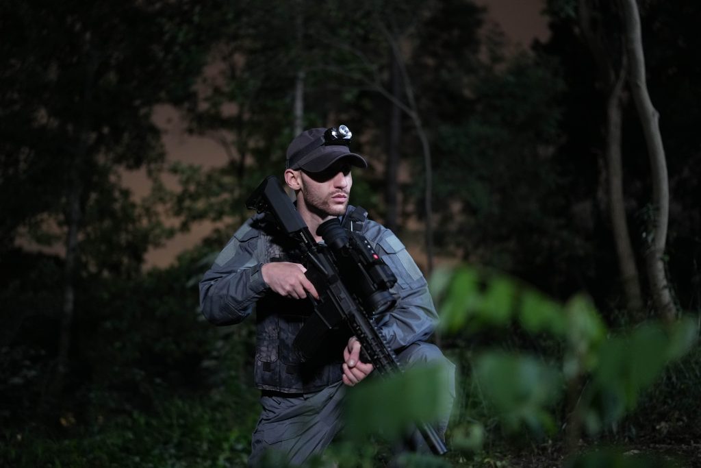 The man crouched in the dark grass with a shotgun